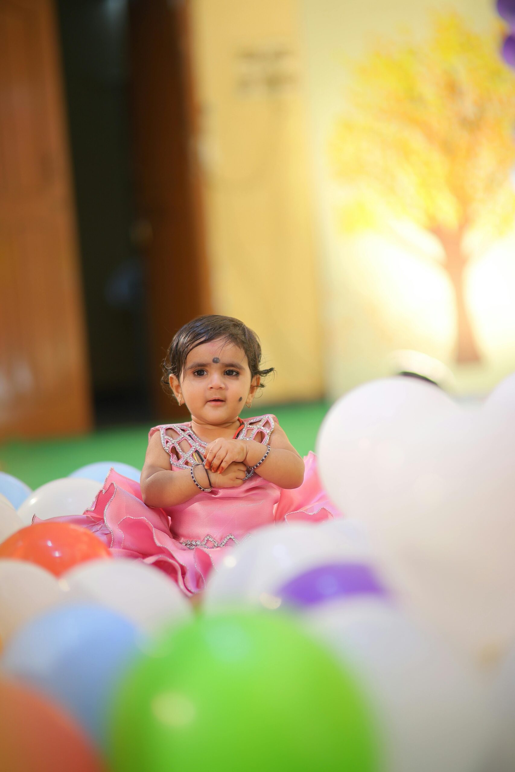 Charming Indian girl enjoying a lively indoor birthday party surrounded by balloons at play school