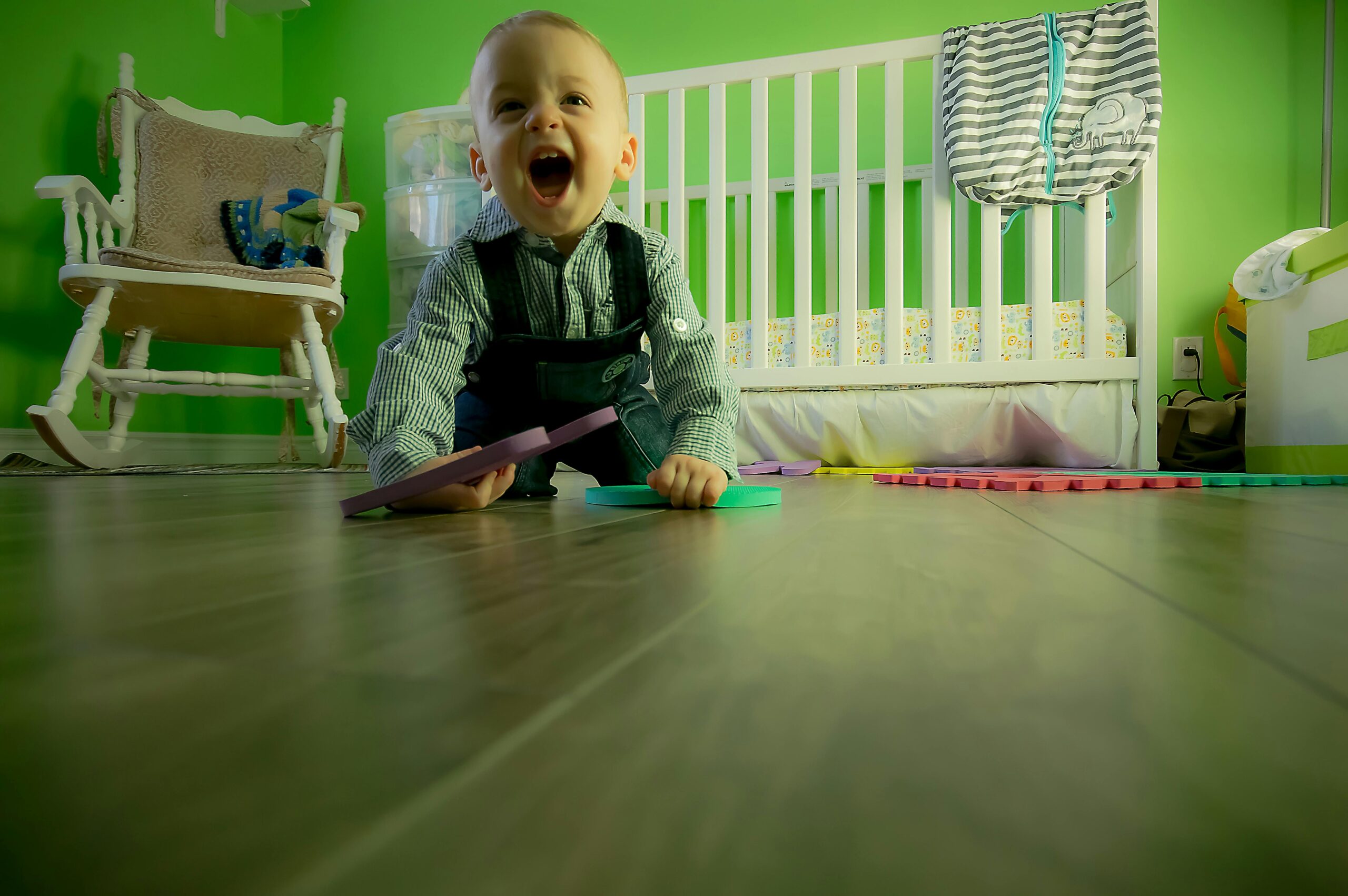 Delightful baby boy crawling on a wooden floor, playing happily in a vibrant green nursery at play school